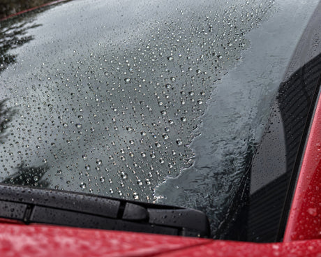 Antipioggia alla prova: gocce che perlano sul vetro sigillato, sul bordo non trattato resta un velo d'acqua