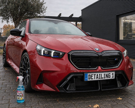 Tugalin Glas-Teufel vor einem roten BMW M5 mit beschlagener Frontscheibe — gezeigt im Artikel „Auto beschlägt von innen: Warum eine saubere Scheibe länger klar bleibt“