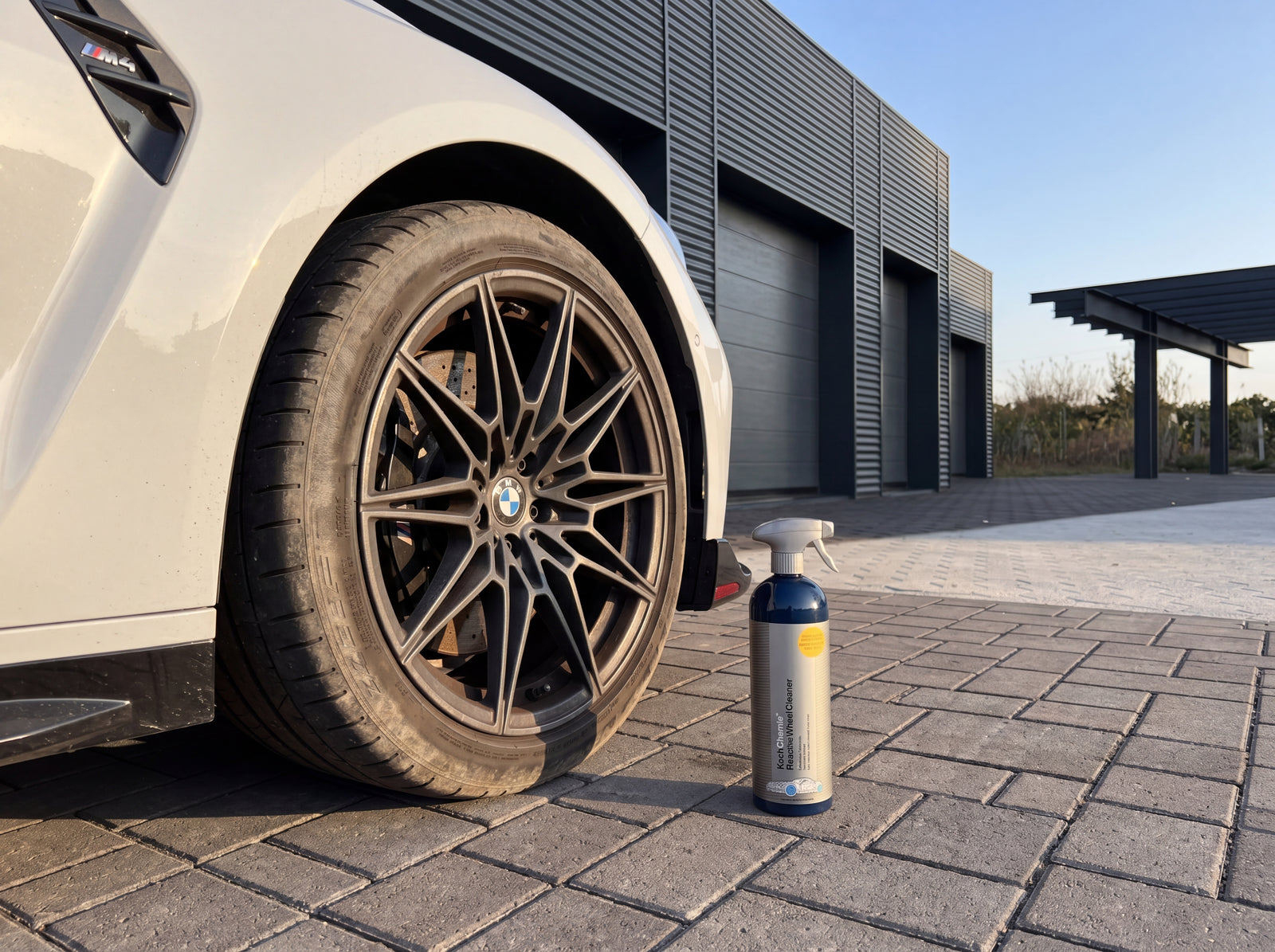 Koch-Chemie Reactive Wheel Cleaner vor der schmutzigen Felge eines weißen BMW M4 CSL auf Pflastersteinen einer Detailing-Werkstatt — ausgangszustand mit Bremsstaub-Kontamination vor der Reinigung